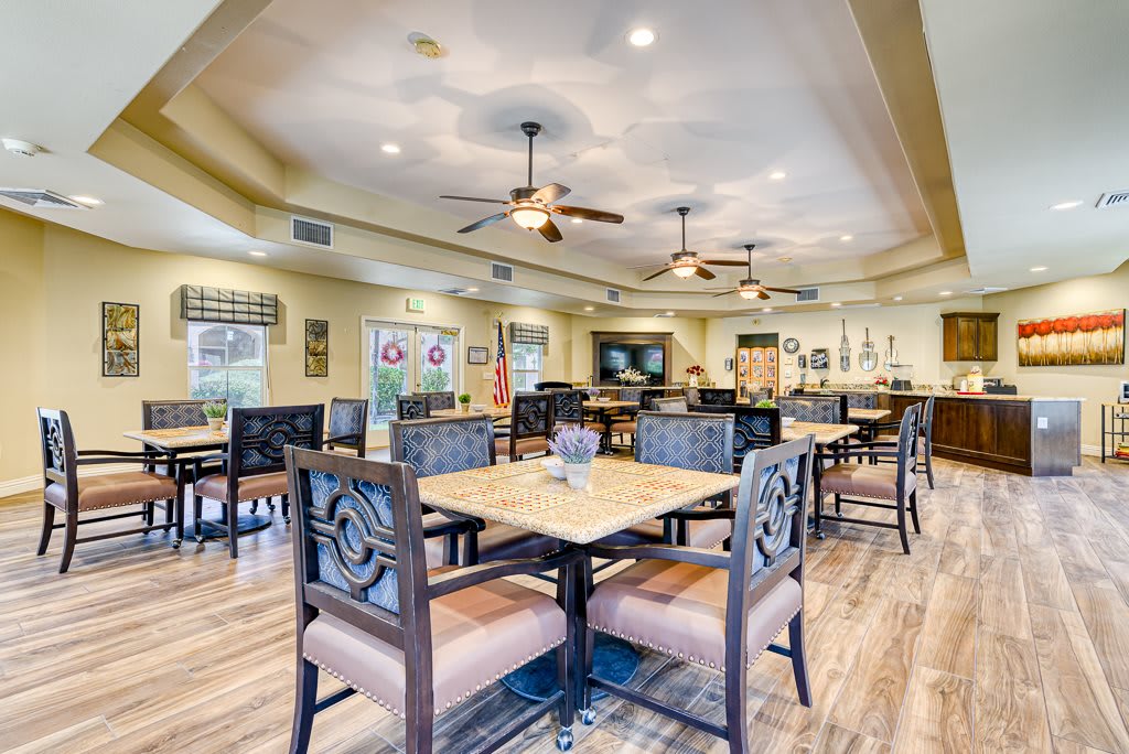 A spacious dining area with multiple tables and chairs, featuring ceiling fans and wooden flooring.