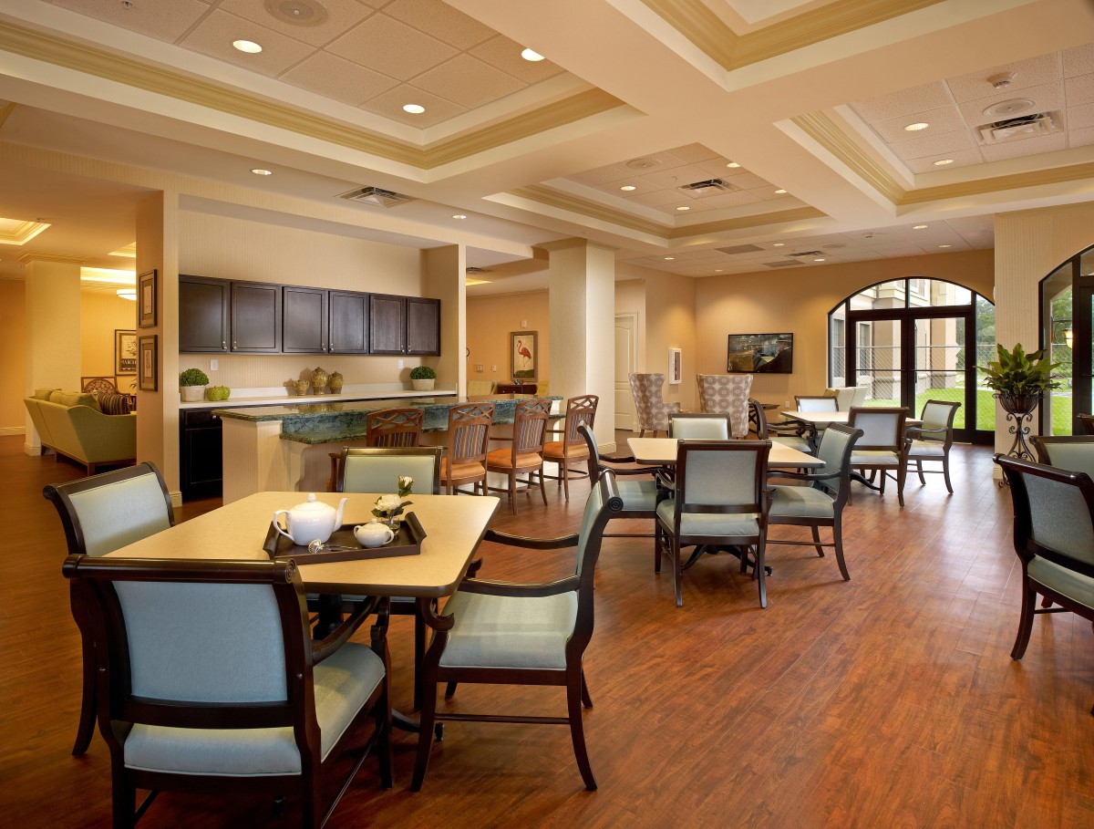 A spacious dining area with multiple tables and chairs, featuring a wooden floor and ceiling lights.