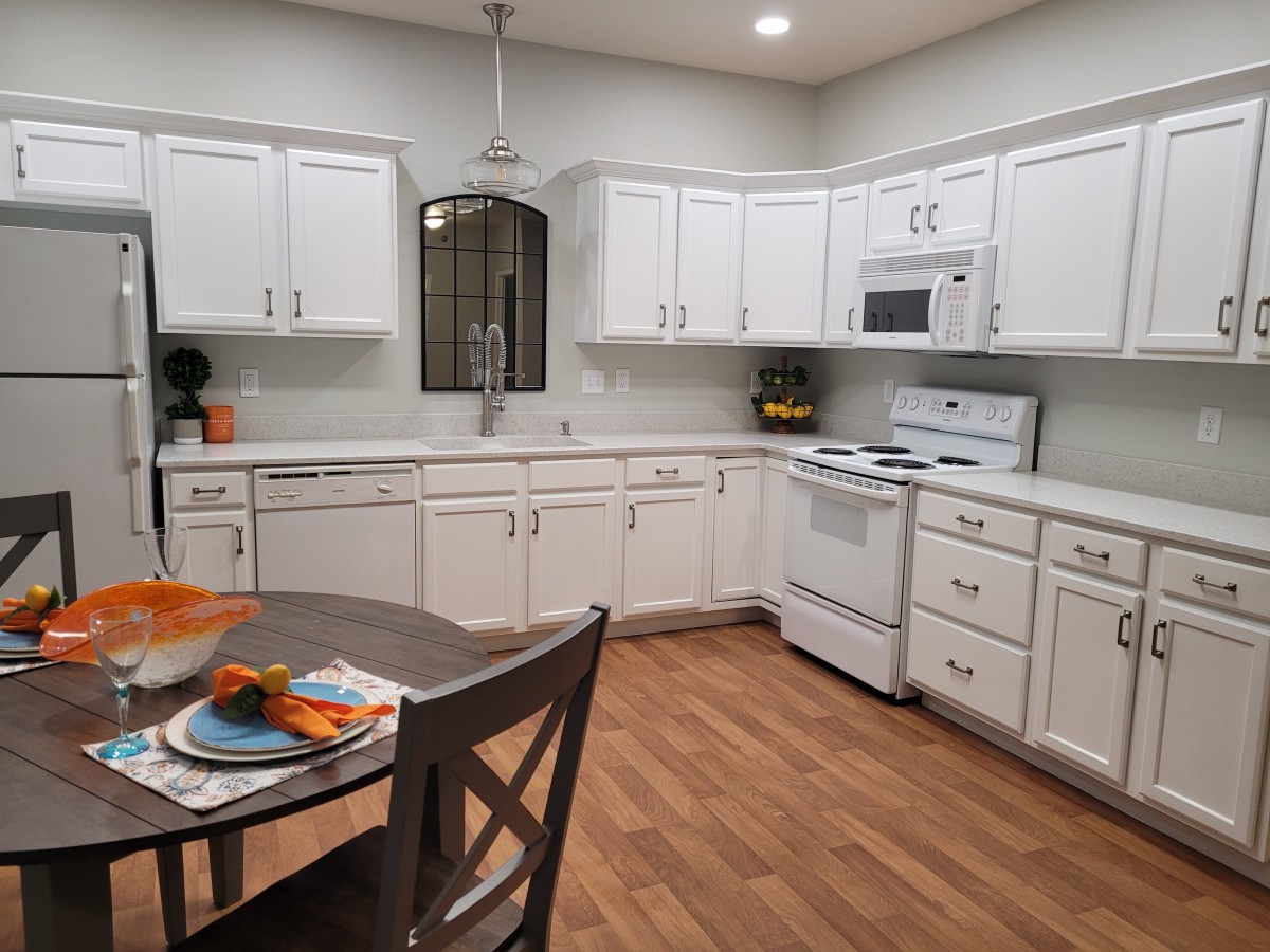 A modern kitchen with white cabinets, a dining table, and wood flooring.