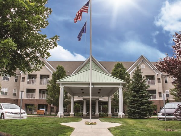 A building entrance with American and state flags, surrounded by trees under a sunny sky.