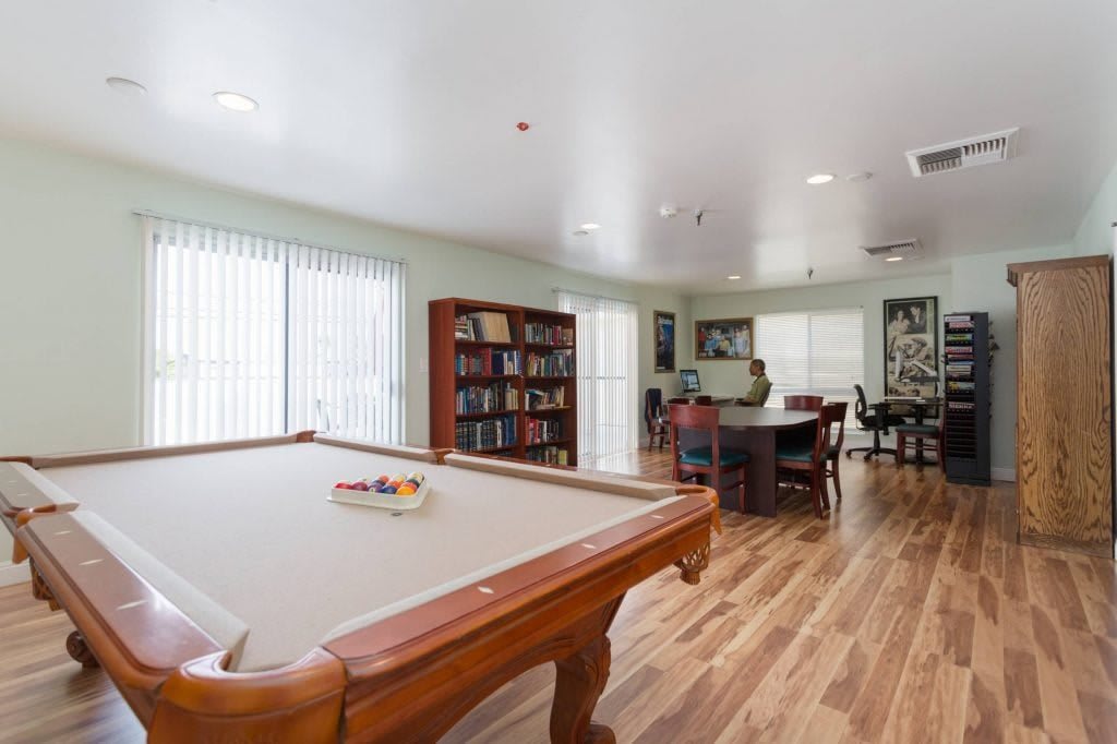 A spacious game room featuring a pool table, bookshelves, and a hardwood floor.