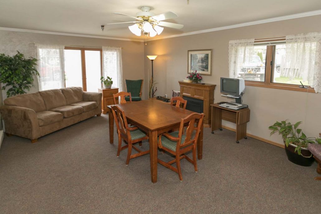 A cozy living room with a dining area, featuring a wooden table surrounded by chairs, a couch, and a computer desk.