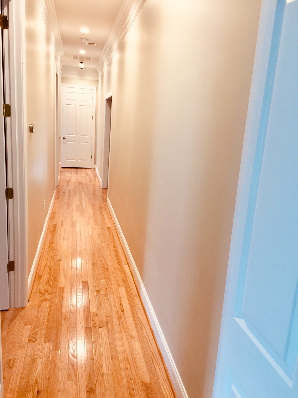 A long, narrow hallway with polished wooden floors and several doors along the sides.