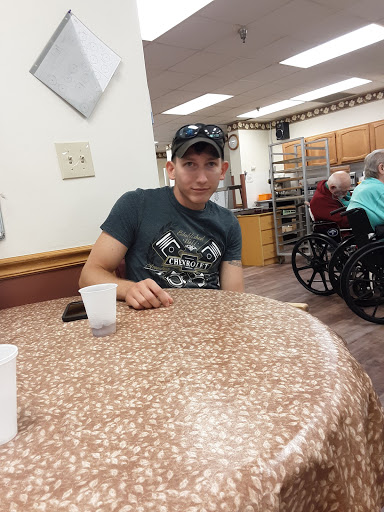 A man sitting at a table in a community center, surrounded by people in wheelchairs.