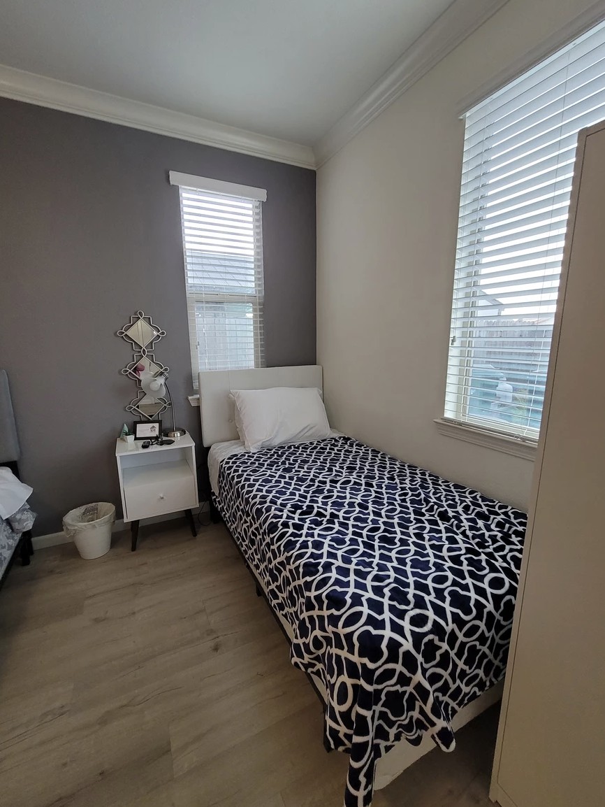 A modern, minimalist bedroom featuring a single bed with patterned bedding and a small nightstand.