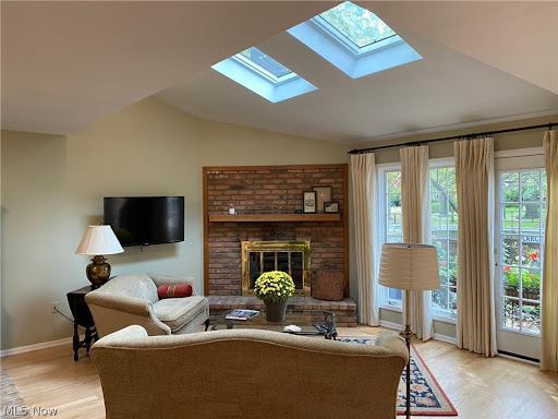 A cozy living room featuring a brick fireplace, skylights, and comfortable seating.