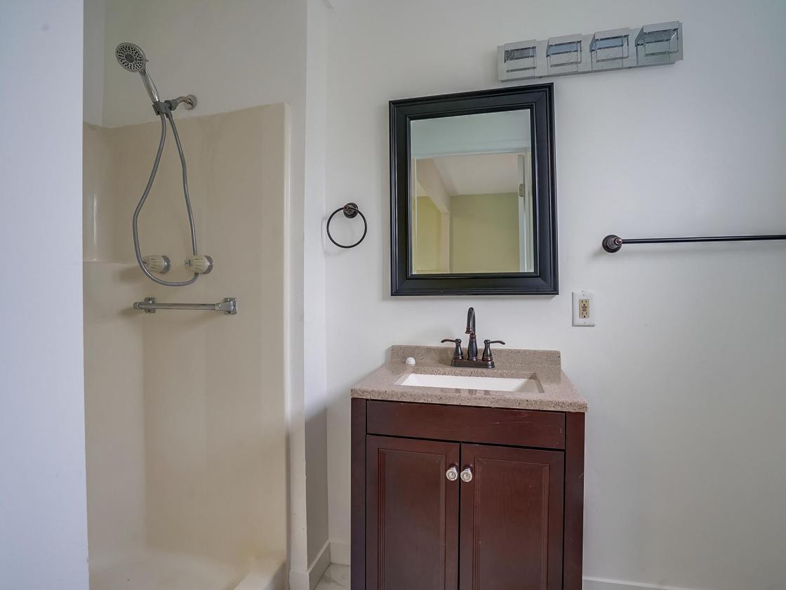 A clean and simple bathroom with a shower, vanity, and mirror.