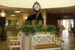 A cozy indoor lobby area with a decorative clock, benches, and greenery.