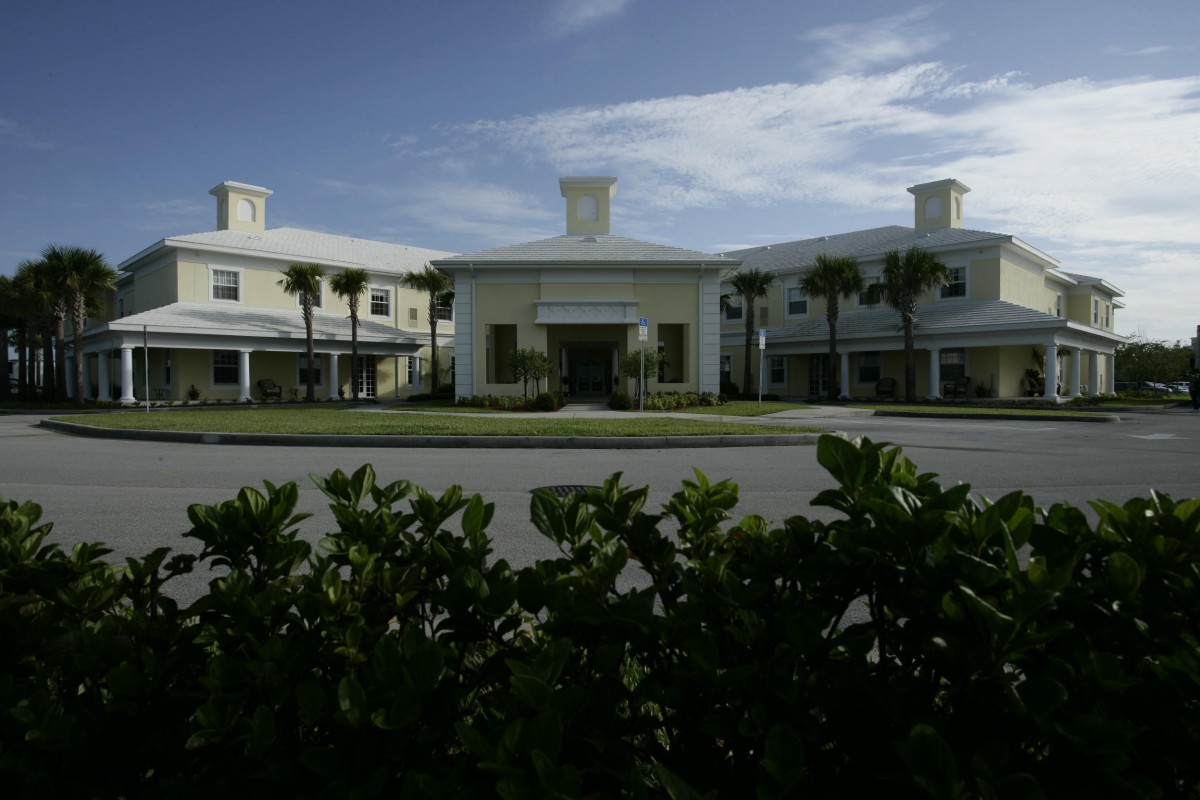 A modern building surrounded by palm trees and greenery under a partly cloudy sky.