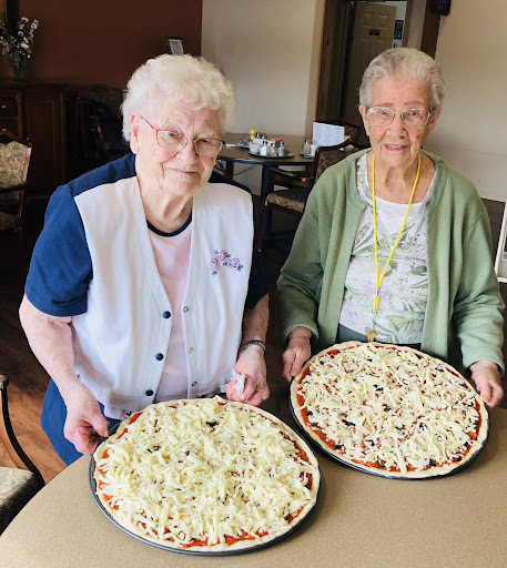 Two women proudly display their homemade pizzas, showcasing their culinary skills and joy.