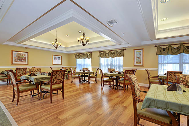 An elegantly designed dining room with multiple tables and chairs, featuring warm lighting and a wooden floor.