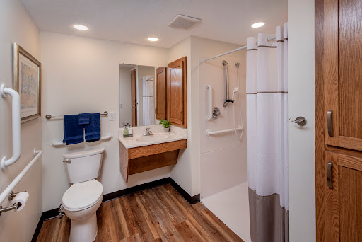 A modern, well-lit bathroom featuring a toilet, sink, and shower area with wooden flooring.