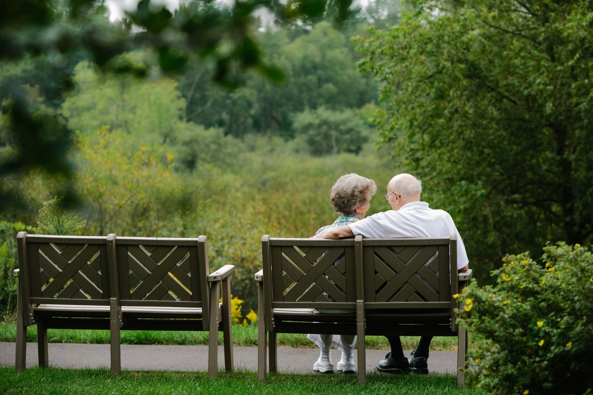 An elderly couple sitting together on a park bench, enjoying the natural surroundings.