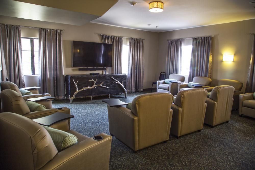 A cozy living room setup with multiple chairs facing a television, surrounded by elegant curtains.