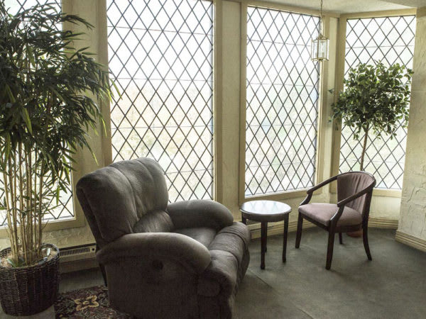 A cozy lounge area featuring a leather armchair, wooden chairs, and large windows with lattice patterns.