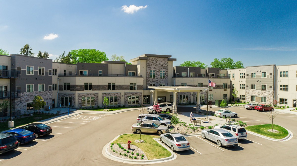 A large building with a parking lot filled with cars on a sunny day.