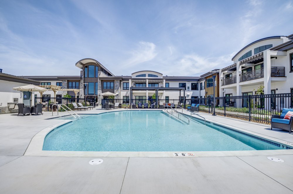 A modern apartment complex with a large outdoor swimming pool under a clear blue sky.