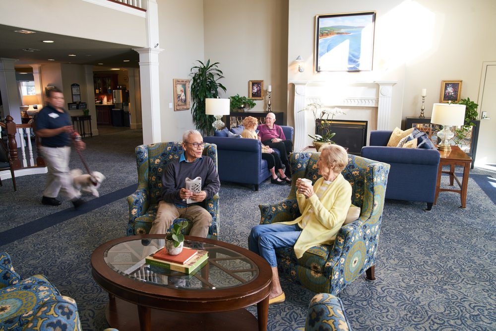 A group of seniors relaxing and conversing in a cozy living room setting with comfortable armchairs and a coffee table.