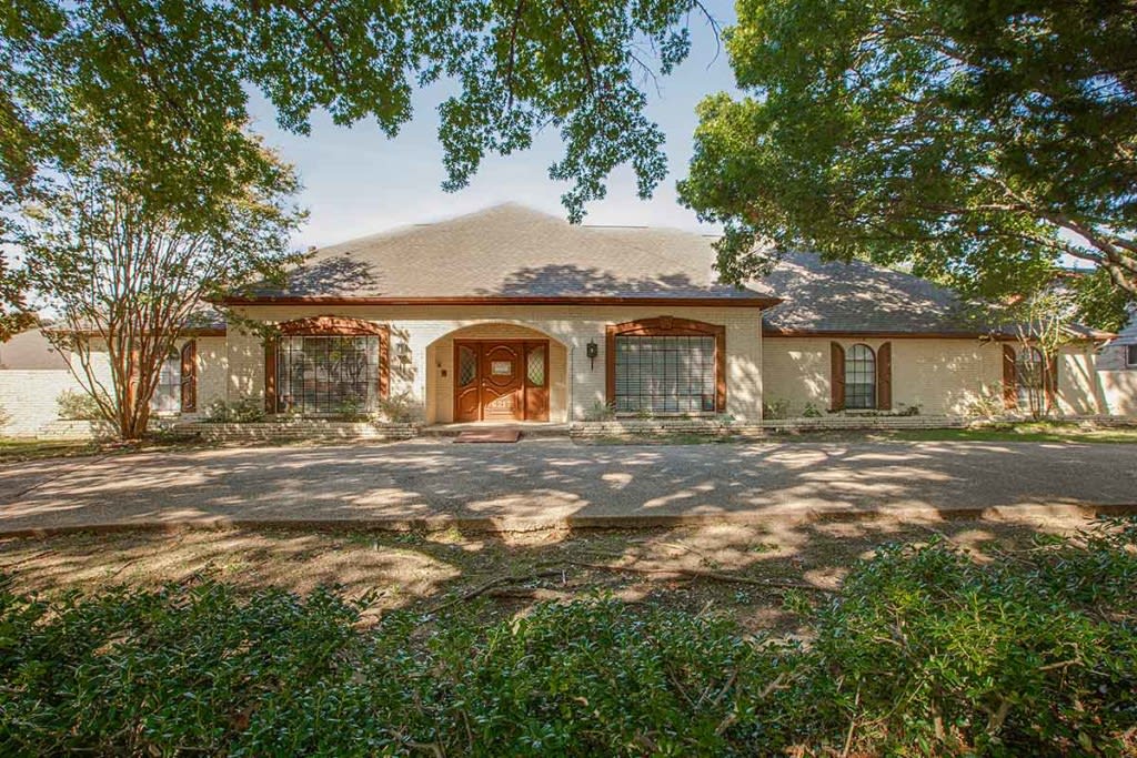 A charming single-story house surrounded by trees and a spacious driveway.
