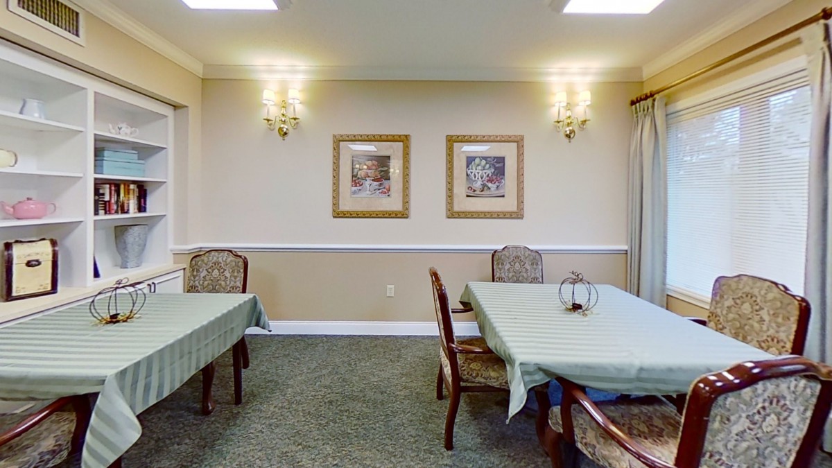 A cozy dining room with neatly arranged tables and chairs, adorned with framed artwork and elegant lighting.