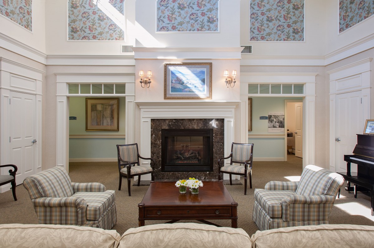 A cozy living room with a fireplace, surrounded by chairs and adorned with artwork and decor.
