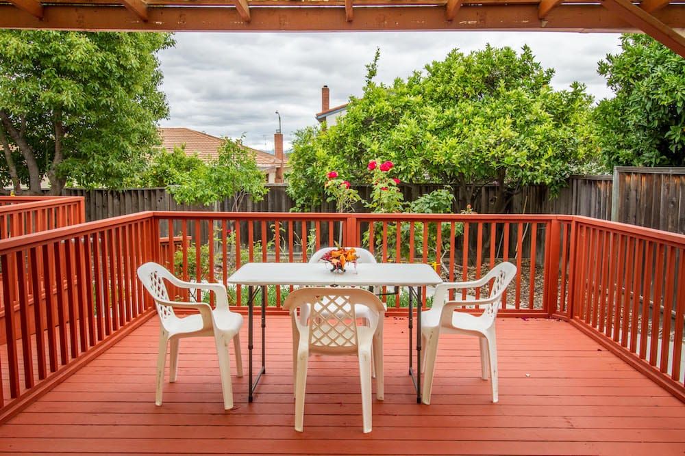 A cozy backyard deck with a table and chairs surrounded by greenery.
