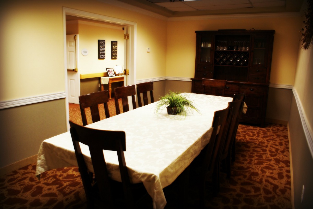 A cozy dining room with a long table and wooden chairs, featuring a potted plant centerpiece.