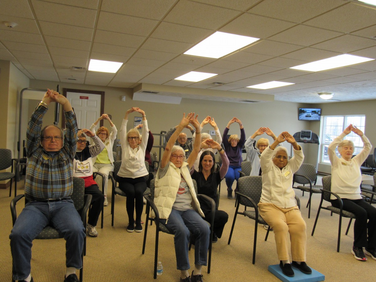 A group of seniors participating in a chair exercise class indoors.