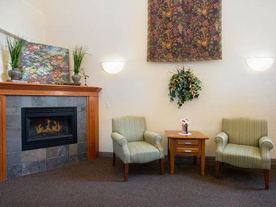 A cozy living room with two armchairs, a wooden side table, and a fireplace adorned with artwork and decorative plants.