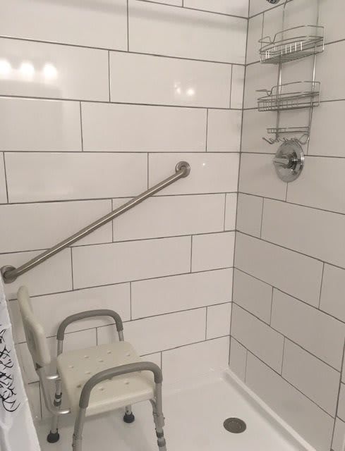 A bathroom shower with a tiled wall, equipped with a grab bar and shower seat for safety.