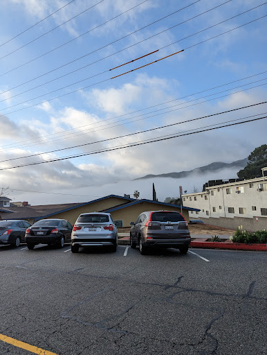 A serene morning view of a parking lot with cars parked and clouds hovering over the mountains in the background.