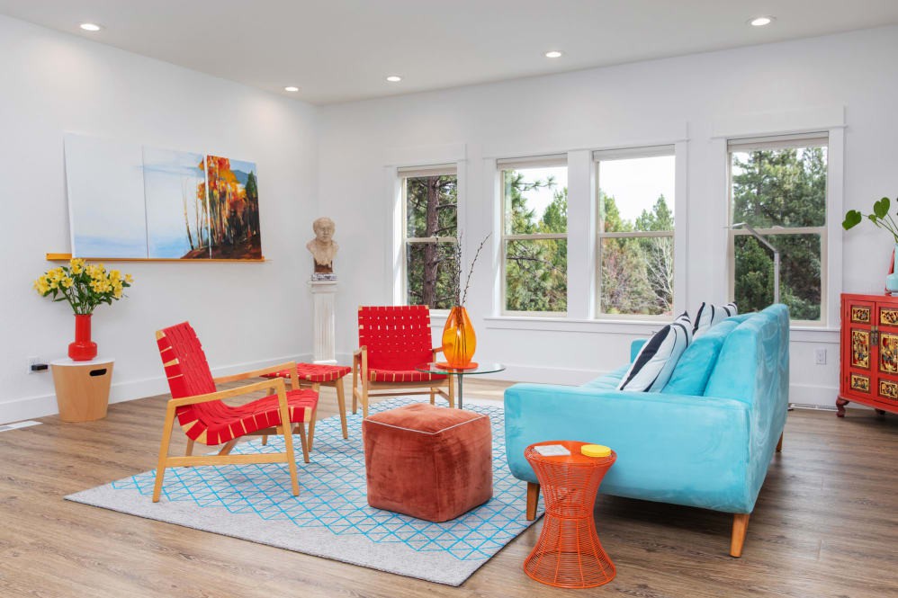 A modern and colorful living room featuring red chairs, a blue sofa, and various decorative elements.