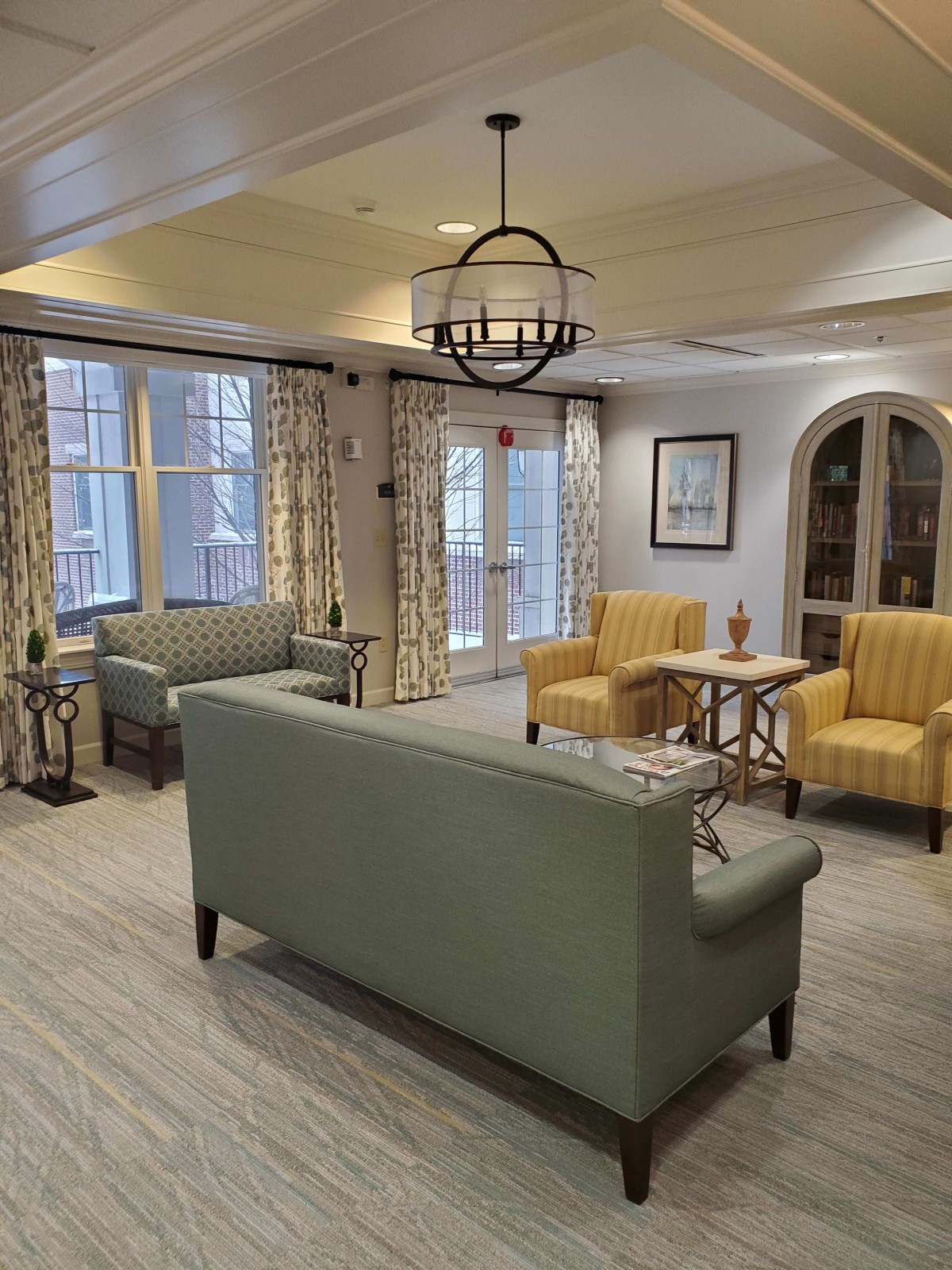 A cozy living room with sofas and armchairs arranged around a central table, featuring elegant curtains and a modern lighting fixture.