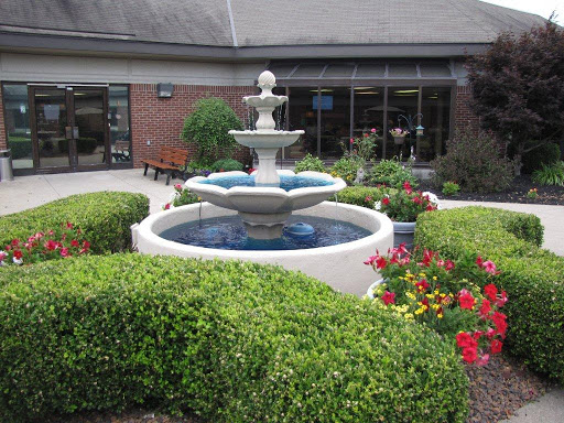 A serene garden scene featuring a multi-tiered fountain surrounded by vibrant flowers and neatly trimmed bushes.