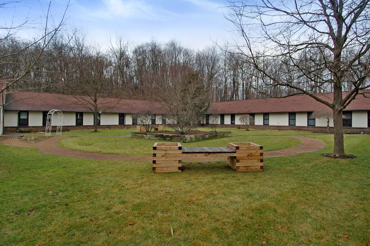 Circular courtyard with buildings and wooden benches surrounded by trees.