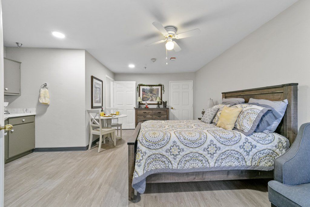 A cozy bedroom with a bed, dining table, and ceiling fan.