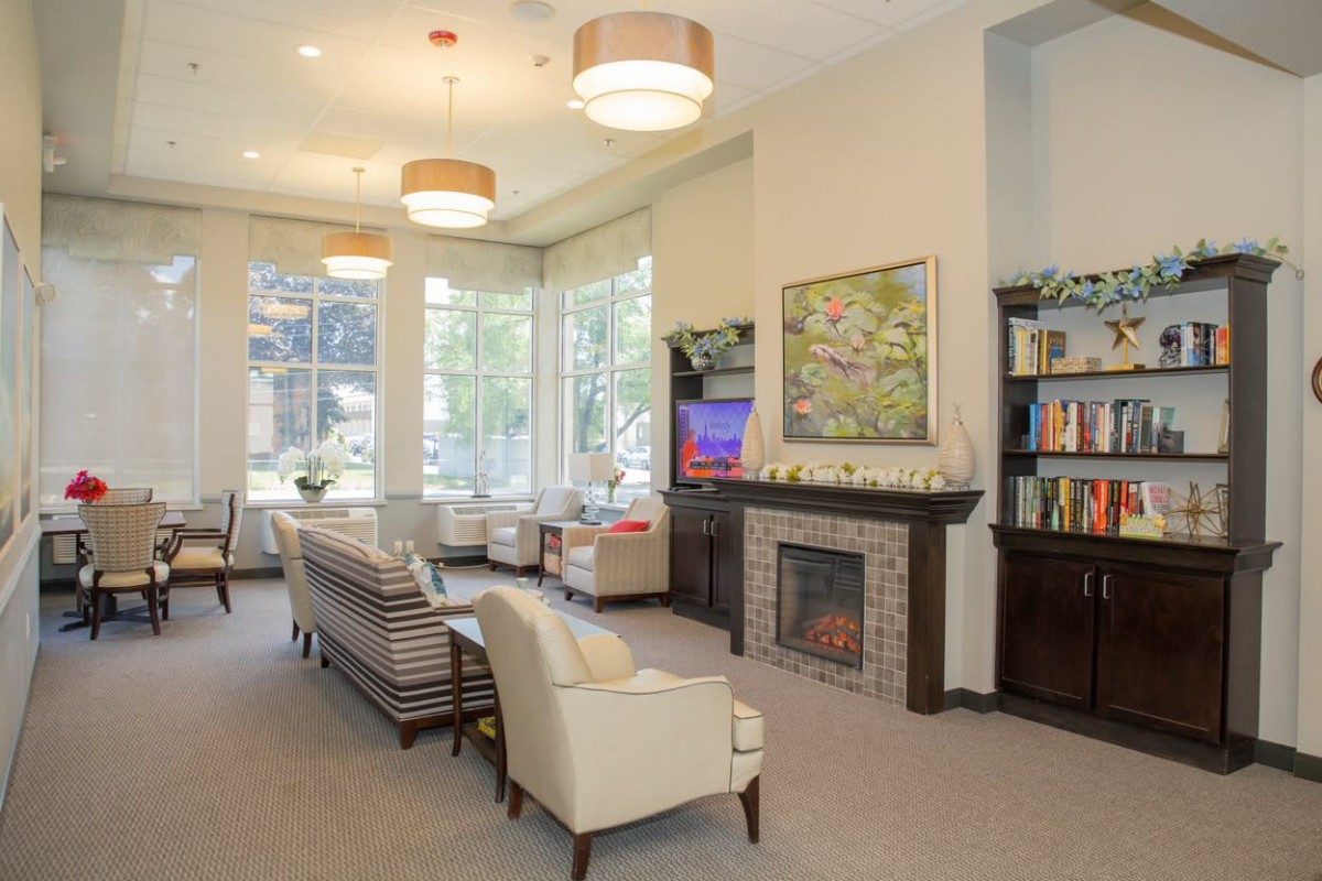 A bright and inviting living room with comfortable seating, a fireplace, bookshelves, and large windows.