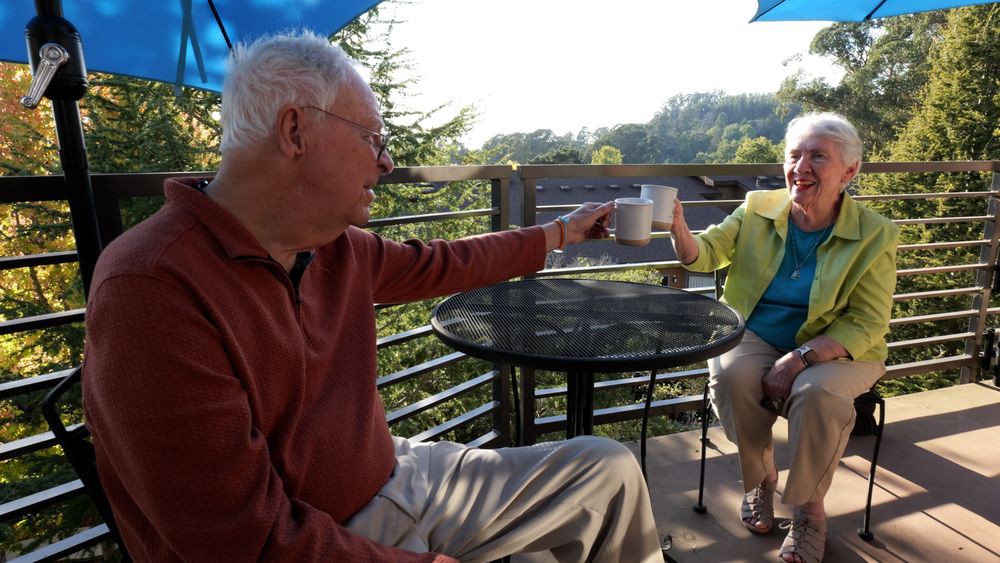 An elderly couple enjoying coffee together on a scenic patio.