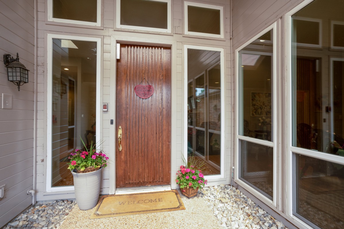 A modern entryway with a wooden front door flanked by large windows and potted plants.