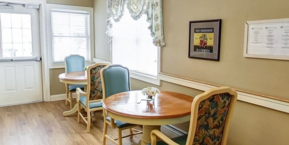 A cozy dining area with round tables and upholstered chairs near a window with elegant curtains.