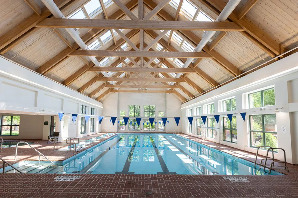 A well-lit indoor swimming pool with wooden beams and skylights.