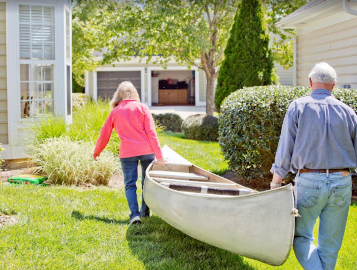 Two people carrying a canoe across a grassy backyard.