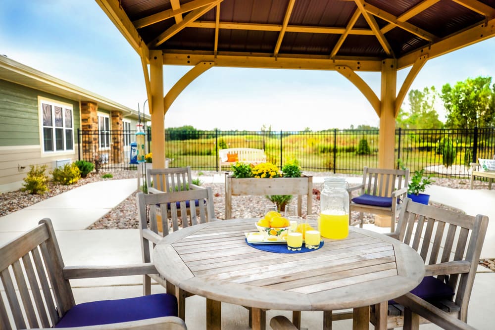 An inviting outdoor patio with a wooden seating area under a gazebo, featuring a table set with lemonade and surrounded by scenic landscape views.