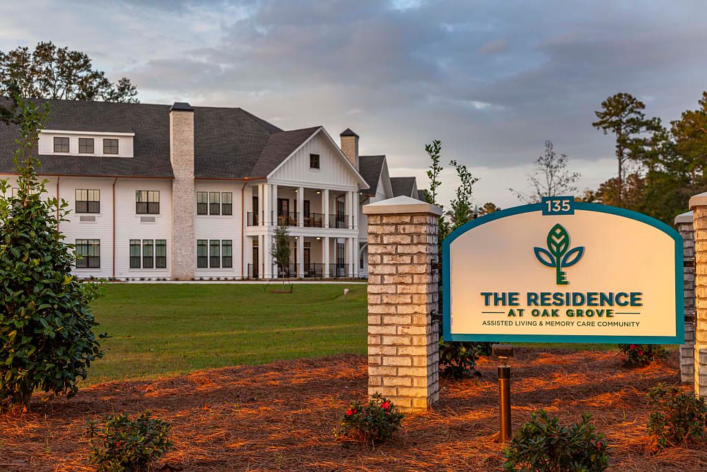 A large residential building with a sign in front, surrounded by a landscaped lawn and trees.