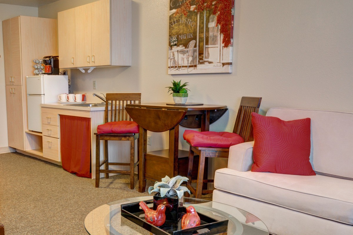 A cozy living and dining area featuring a wooden table, red cushioned chairs, a comfortable sofa with pillows, and stylish decorative elements.