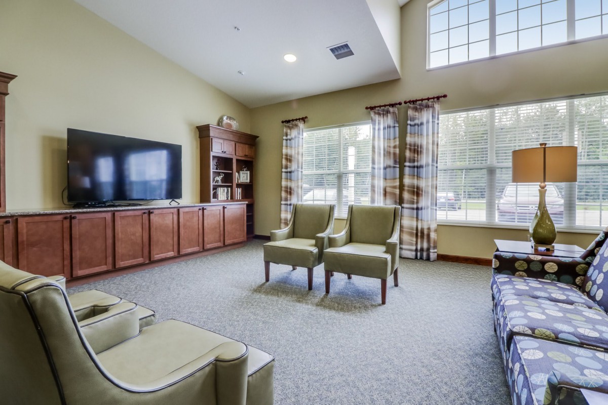 A spacious living room with a television, chairs, and large windows.