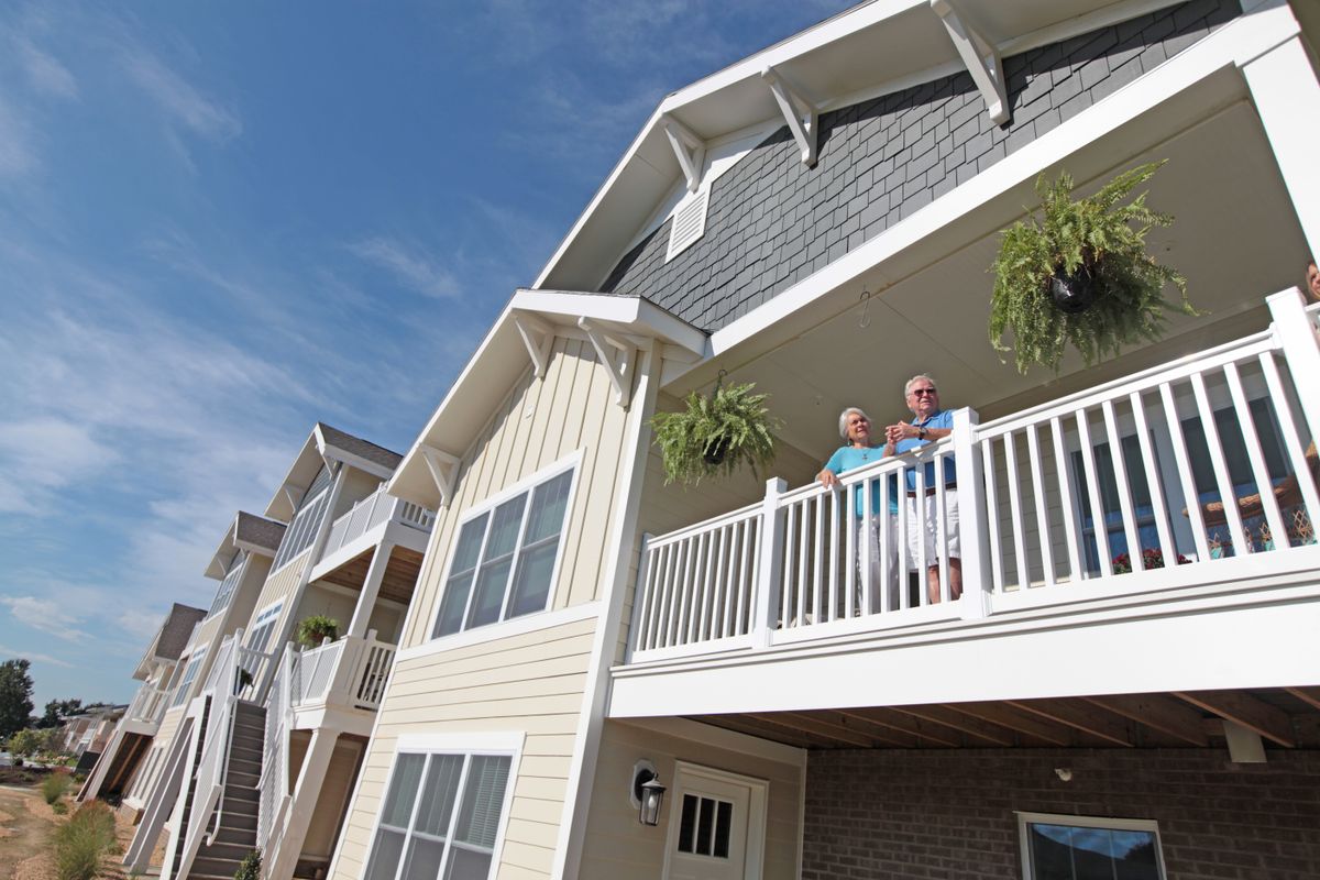 Two people standing on the balcony of a residential building with hanging plants.