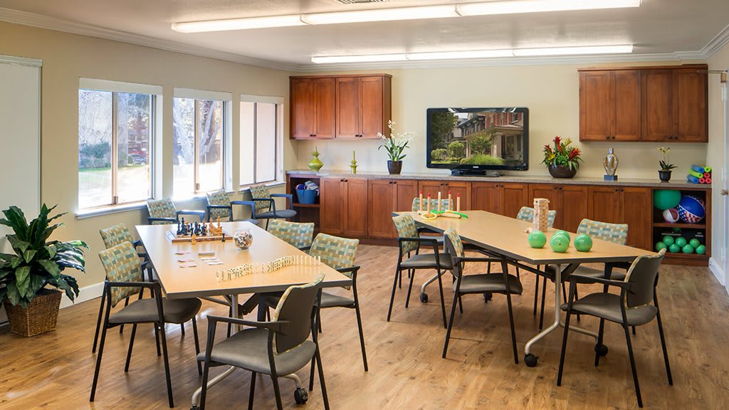 A well-lit classroom with tables, chairs, and a television for learning activities.