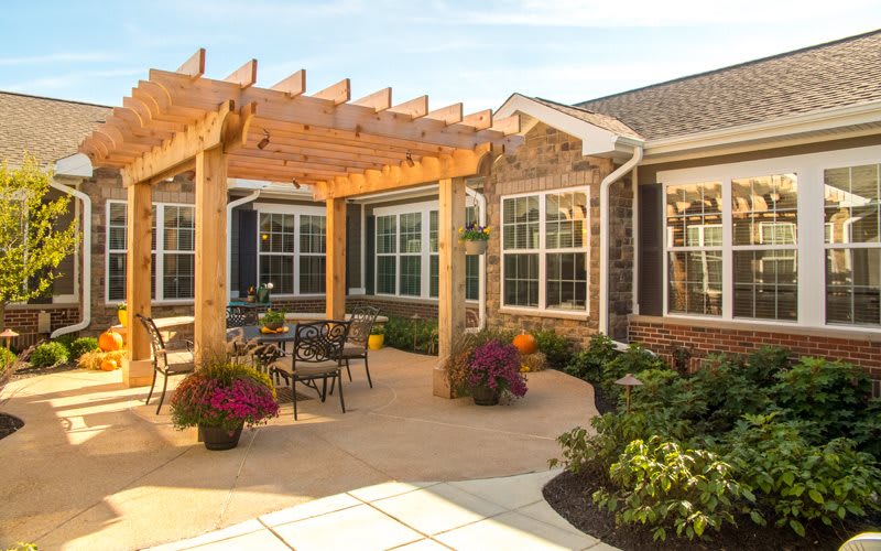 A cozy patio with a wooden pergola, outdoor seating, and vibrant flowers surrounded by a brick house.