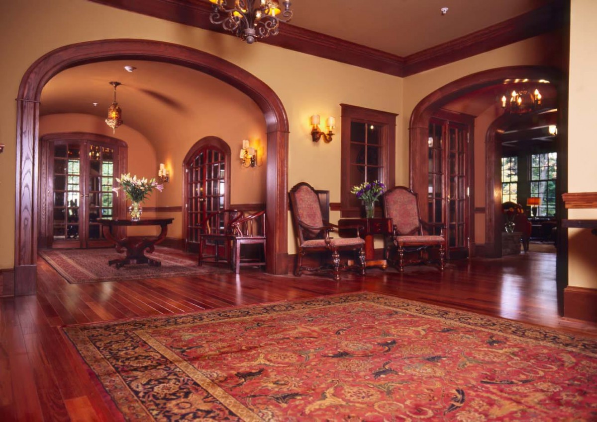 A grand lounge featuring traditional decor with wooden flooring, elegant arched doorways, and a large area rug.
